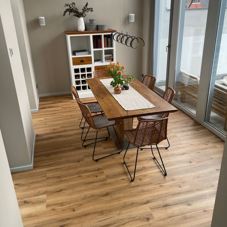 Klick-Vinylboden in Braun in Esszimmer mit Esstisch und braunen Stühlen, Tischdecke, Schrank mit Bucüchern und Pflanzen