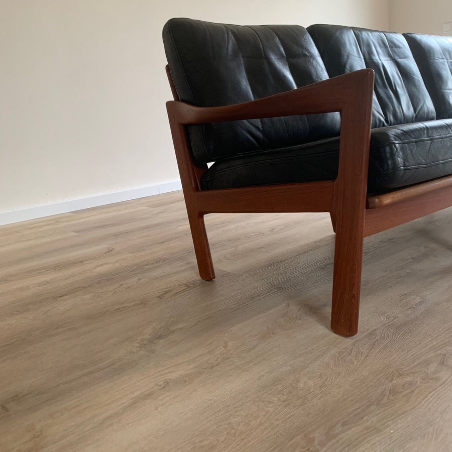Klebevinyl Eiche Mirandus in heller Holzoptik mit dunkler Holzcouch mit schwarzen Lederpolstern – hochwertiger Vinylboden vom Laminat Fachhandel Laminatshop24